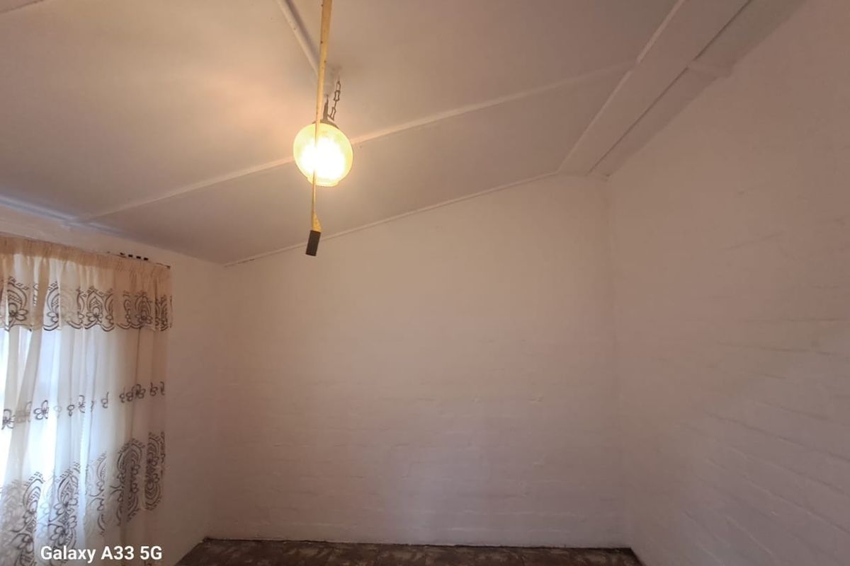 A simple, empty bedroom featuring painted brick walls, a sloped ceiling, and dated flooring, offering a blank canvas for renovation.
