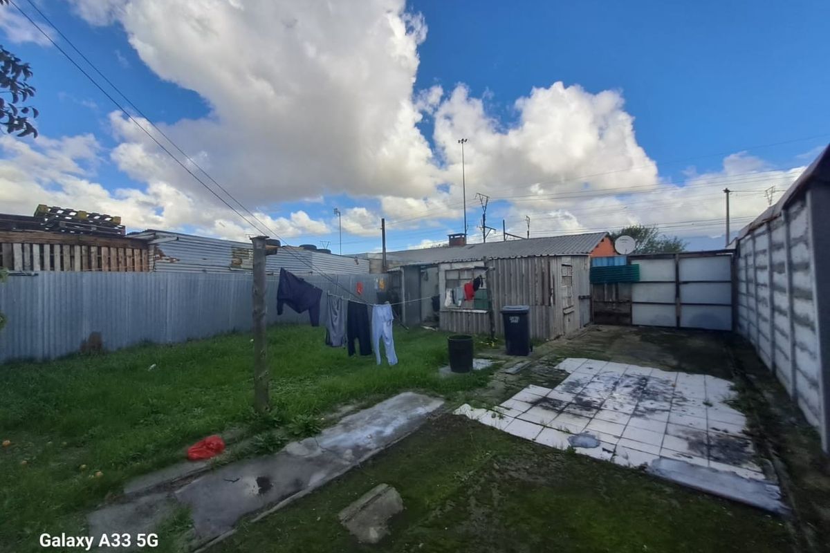 A rear garden area featuring a lawn, paved section, and corrugated metal boundary fencing with an outbuilding structure.