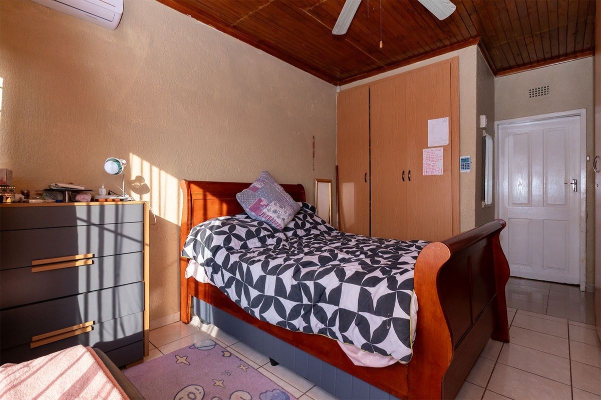 A bedroom featuring built-in wooden cupboards, tiled flooring, and a timber-paneled ceiling with a mounted ceiling fan and air conditioning unit.