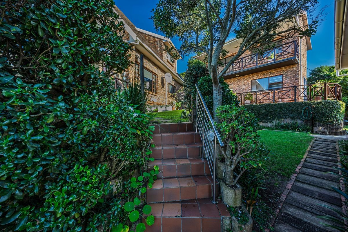 A well-maintained rear exterior view featuring a brick facade, tiled staircase with stainless steel handrails, and a landscaped garden with balcony access.