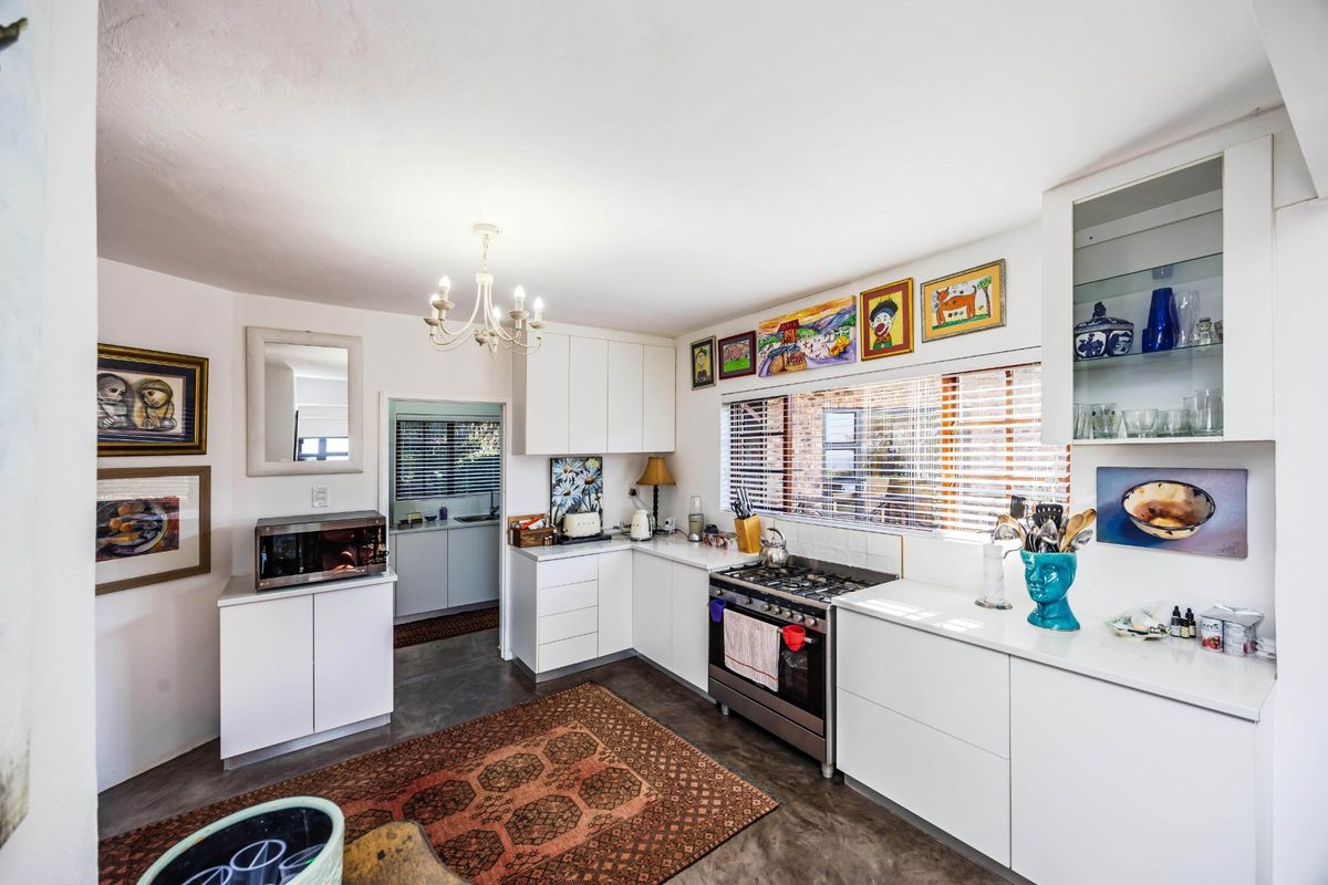A bright, modern kitchen featuring white cabinetry, a gas stove, and polished concrete floors, with an adjacent scullery area visible.