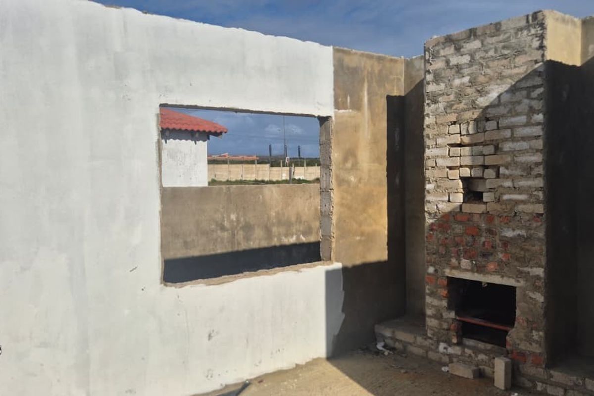 An unfinished interior space featuring exposed brickwork, a fireplace structure, and an open window aperture, currently in the construction phase.