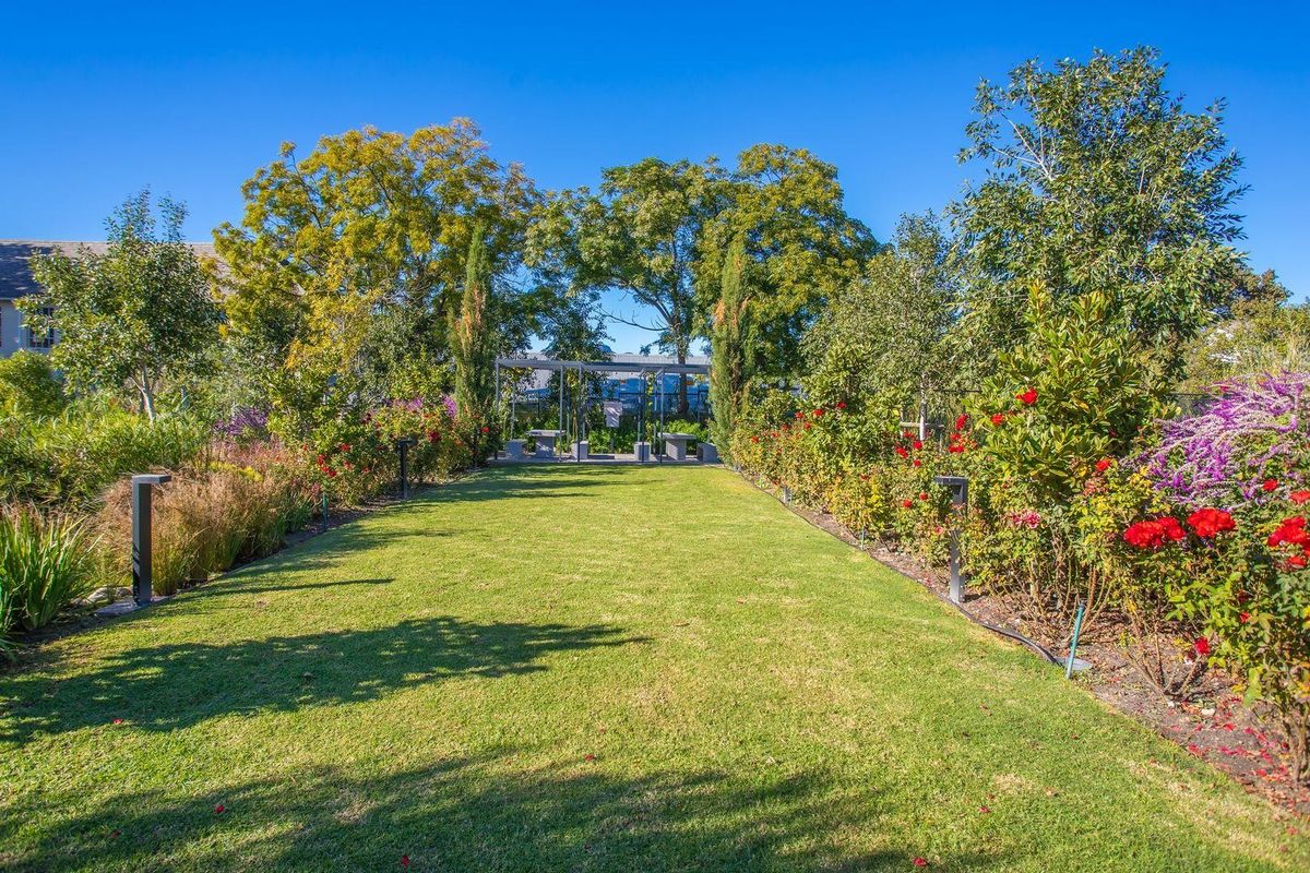 A beautifully landscaped garden featuring a manicured lawn, vibrant flower beds, mature trees, and modern path lighting.