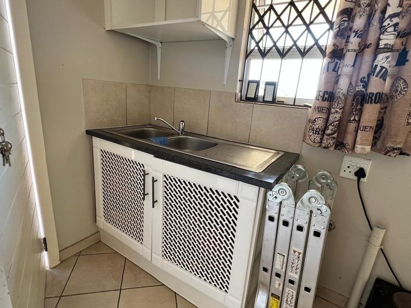 A functional laundry area featuring a stainless steel sink, tiled splashback, and white cabinetry with decorative mesh doors.