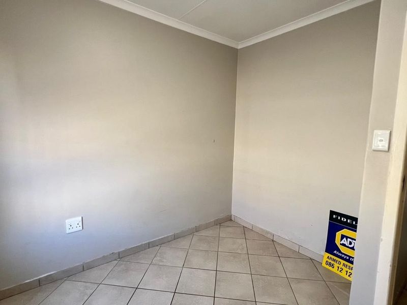 A neutral-toned, empty room featuring tiled flooring and a corner layout, suitable for use as a bedroom or home office.