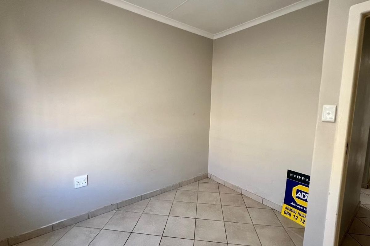 A neutral-toned, empty room featuring tiled flooring and a corner layout, suitable for use as a bedroom or home office.