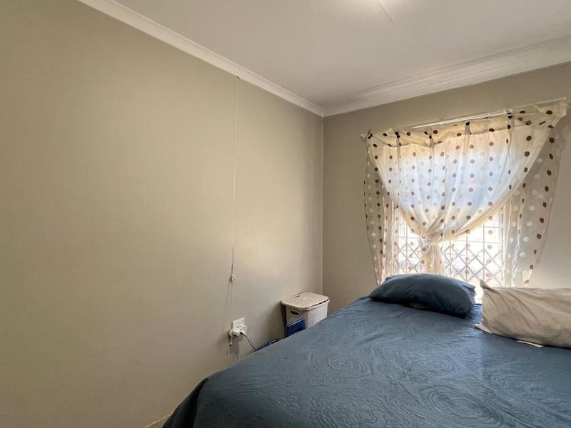 A standard bedroom featuring neutral wall paint, coved cornicing, and a window fitted with security bars.