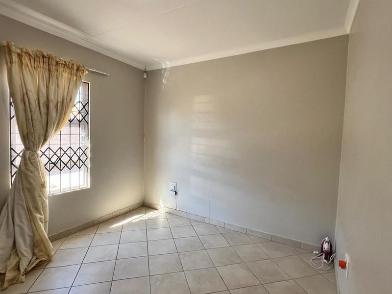 A bright, neutral-toned bedroom featuring tiled flooring, a security-grilled window, and coved ceiling detailing.