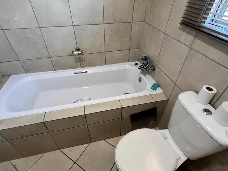 A functional bathroom featuring a built-in bathtub with tiled surround and a standard white toilet.