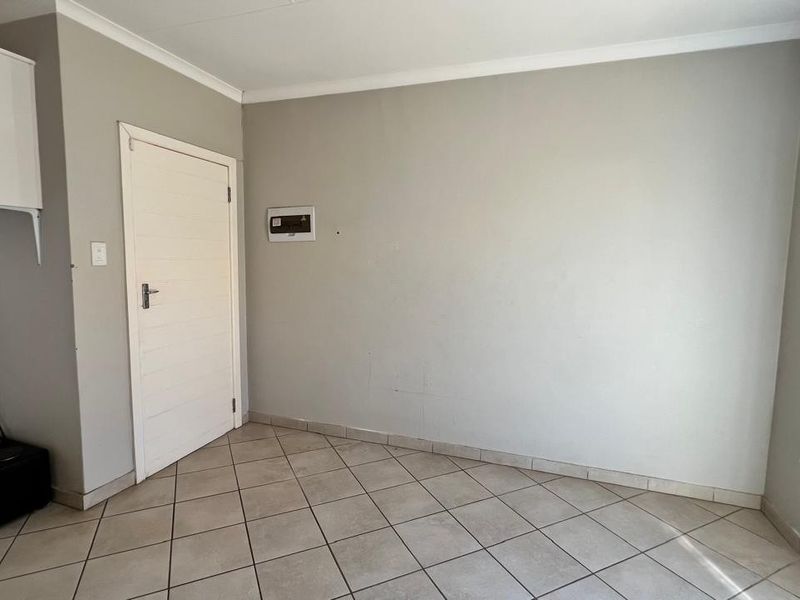 A neutral-toned interior space featuring tiled flooring, a white door, and a wall-mounted electrical distribution board.