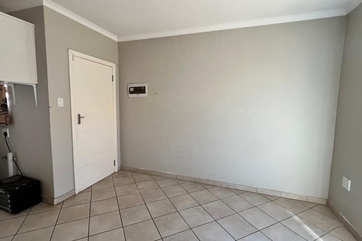 A neutral-toned interior space featuring tiled flooring, a white door, and a wall-mounted electrical distribution board.