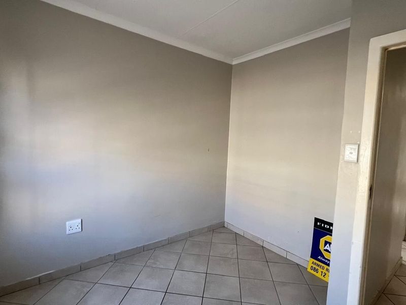 A neutral-toned room featuring tiled flooring and a doorway leading to an adjacent space, offering a clean and versatile area.
