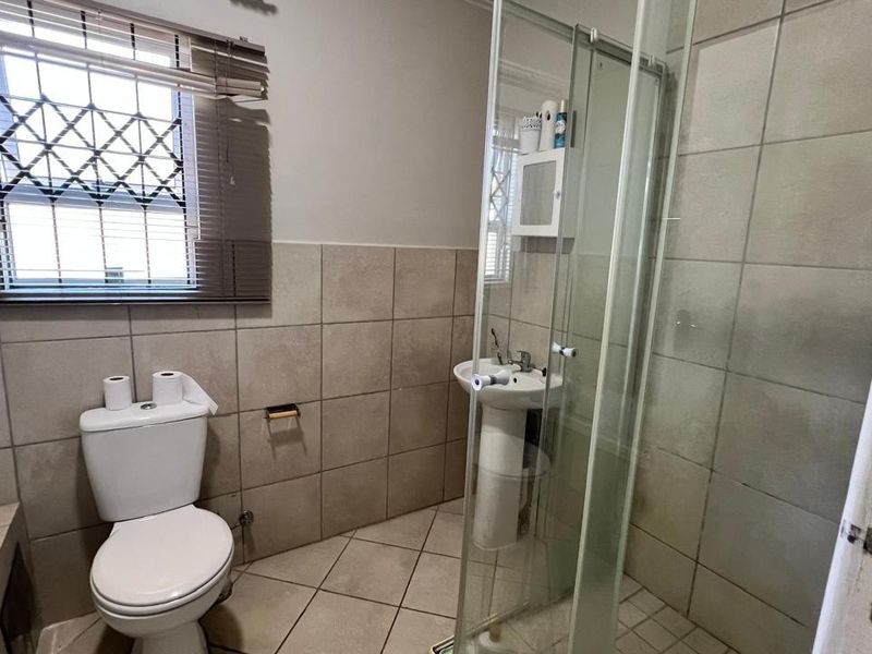 A functional bathroom featuring a pedestal basin, a toilet, and a glass-enclosed shower with neutral wall and floor tiling.