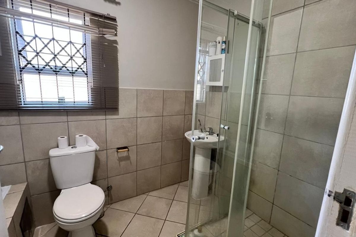 A functional bathroom featuring a pedestal basin, a toilet, and a glass-enclosed shower with neutral wall and floor tiling.