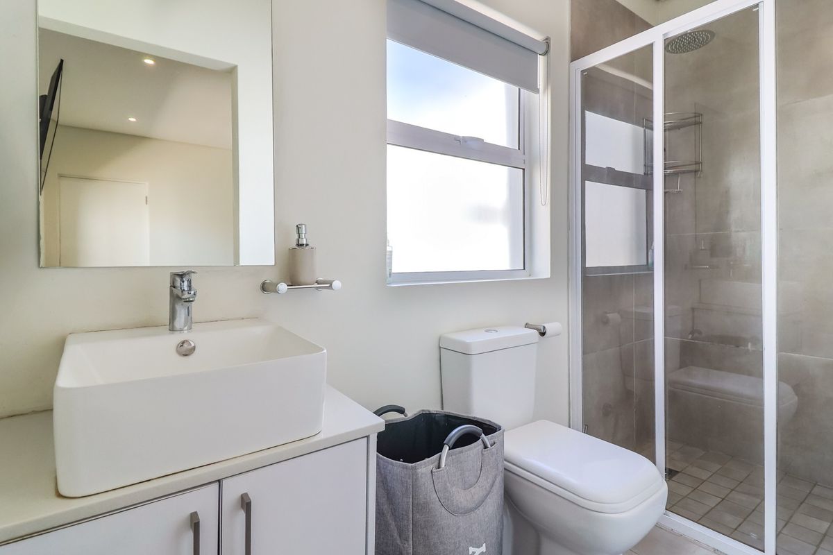 A modern bathroom featuring a vessel sink vanity, a wall-mounted mirror, a toilet, and a glass-enclosed shower with tiled walls.