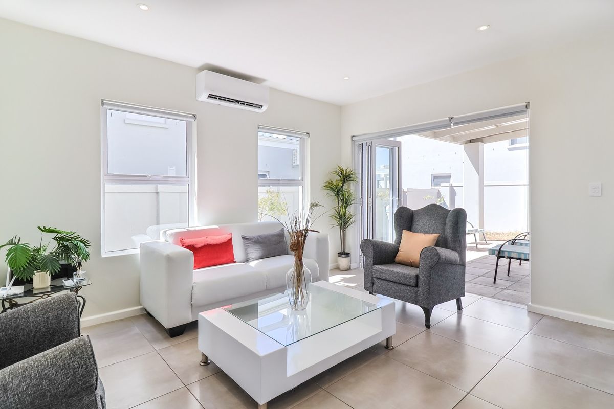 Bright living room featuring large format floor tiles, recessed downlighting, wall-mounted air conditioning unit, and seamless access to an outdoor patio through folding doors.