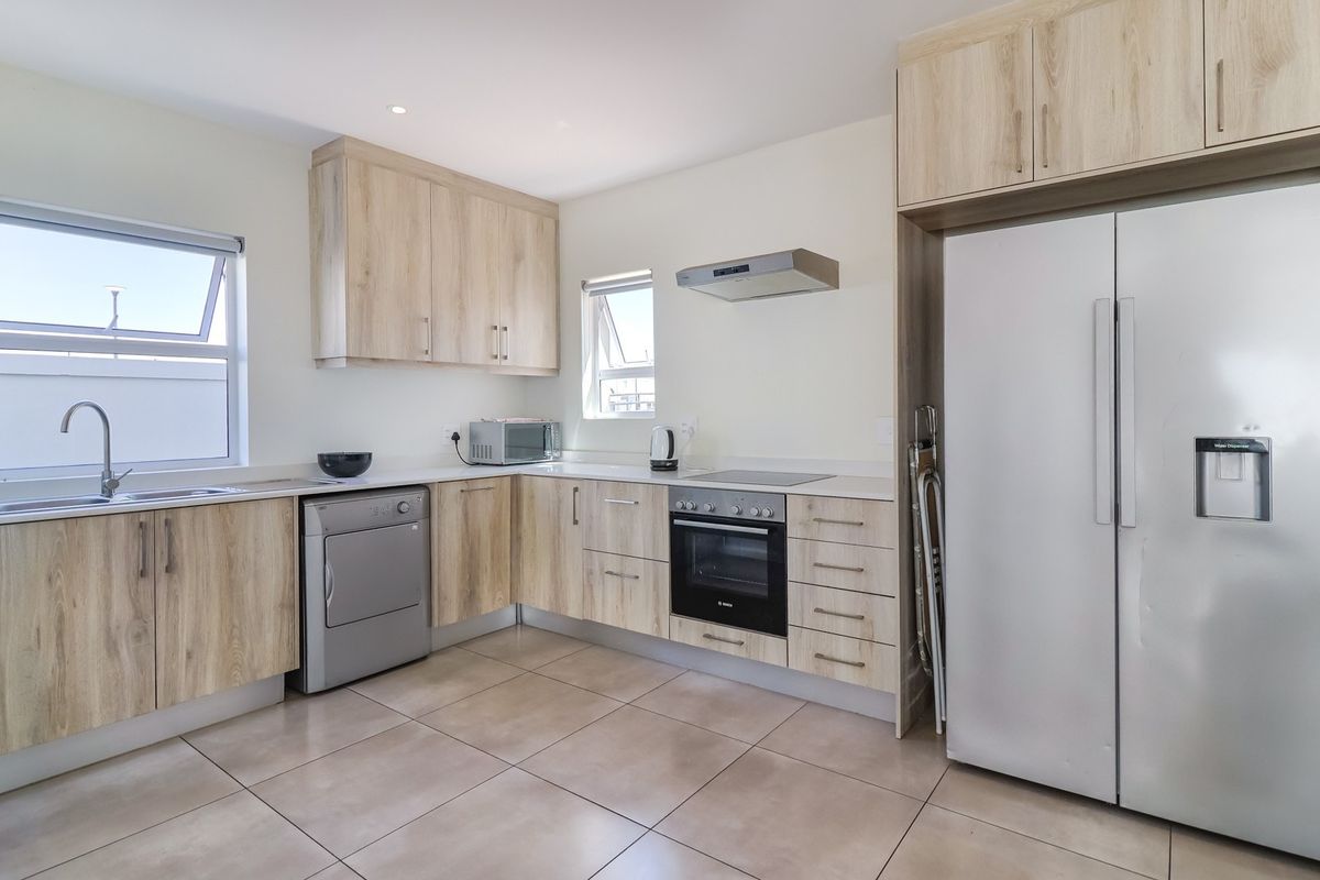 Modern kitchen featuring light wood-grain cabinetry, stone-look countertops, integrated oven, hob, and extractor fan with tiled flooring.