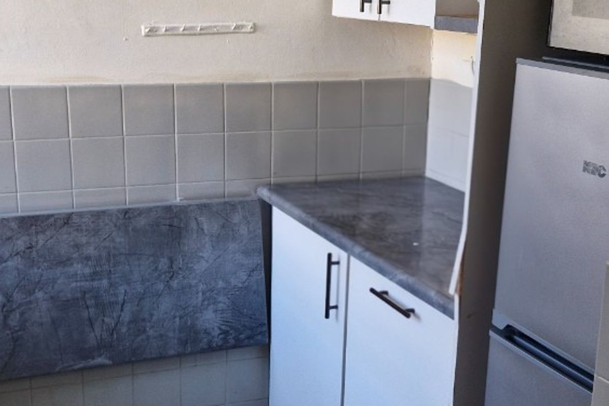 A compact kitchen area featuring white cabinetry, grey stone-look countertops, tiled splashbacks, and tiled flooring.