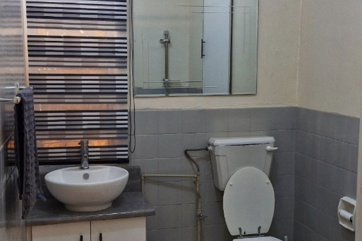 A functional bathroom featuring a vanity basin, toilet, and tiled finishes, providing essential amenities for the property.