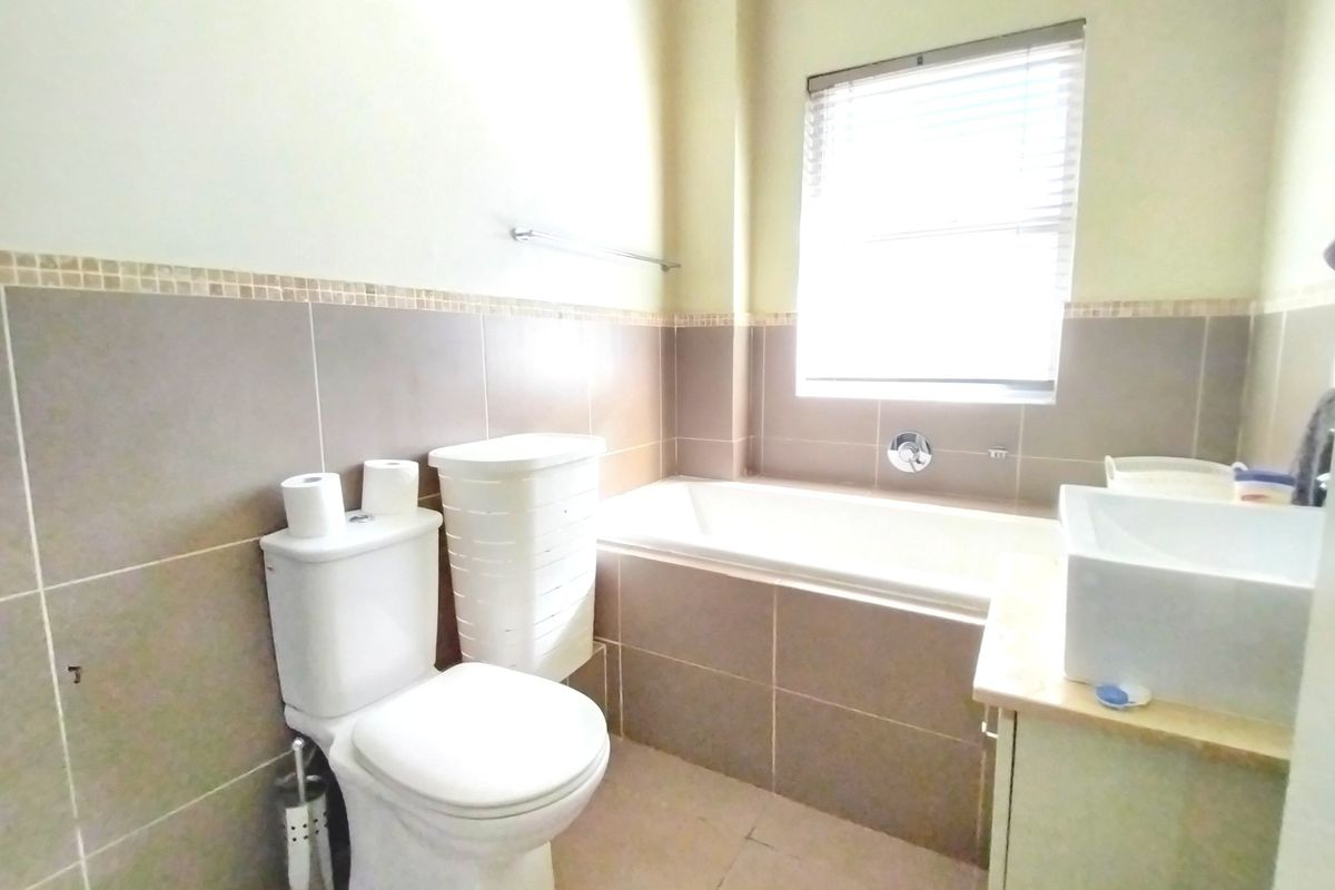 A functional bathroom featuring a built-in bathtub, a modern vanity, and neutral wall tiling with a window for natural light.