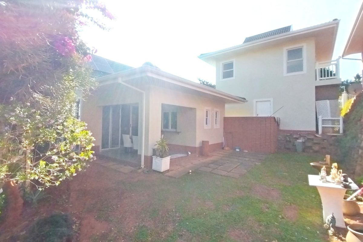 A rear view of the property featuring a covered patio area, brick retaining wall, and a landscaped garden space.