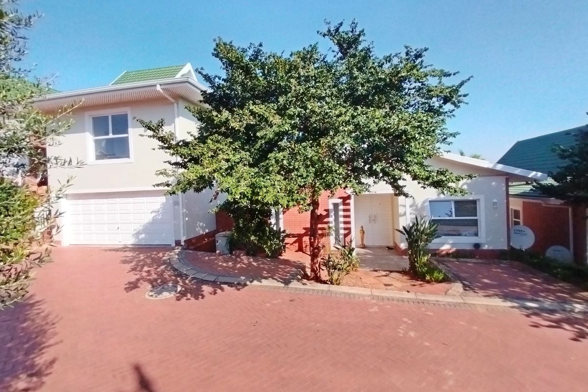 Front exterior view of a two-story house featuring a paved driveway, integrated garage, and a mature tree in the front garden area.