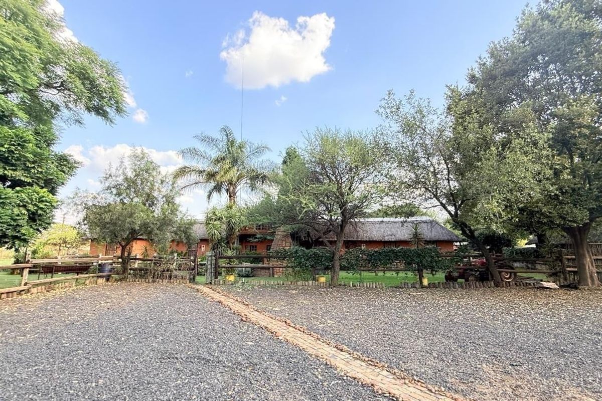 A rustic small holding property featuring a thatched roof dwelling, mature garden landscaping, and a gravel driveway with a brick walkway.