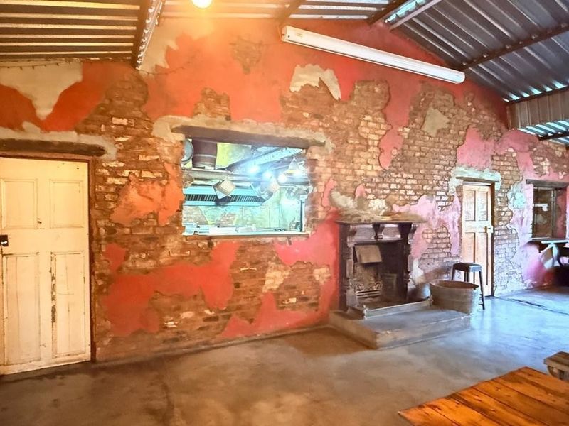 Rustic open-plan space featuring exposed brick walls, a traditional fireplace, and a serving hatch, offering a unique industrial-style character with significant renovation potential.