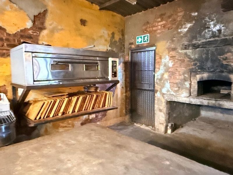 A rustic utility space featuring an industrial oven, a traditional masonry oven, and exposed brick walls, suitable for a bakery or specialized food preparation area.