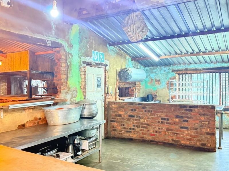 Rustic kitchen area featuring exposed brick walls, corrugated metal roofing, and a brick service counter, requiring significant cosmetic renovation and finish upgrades.