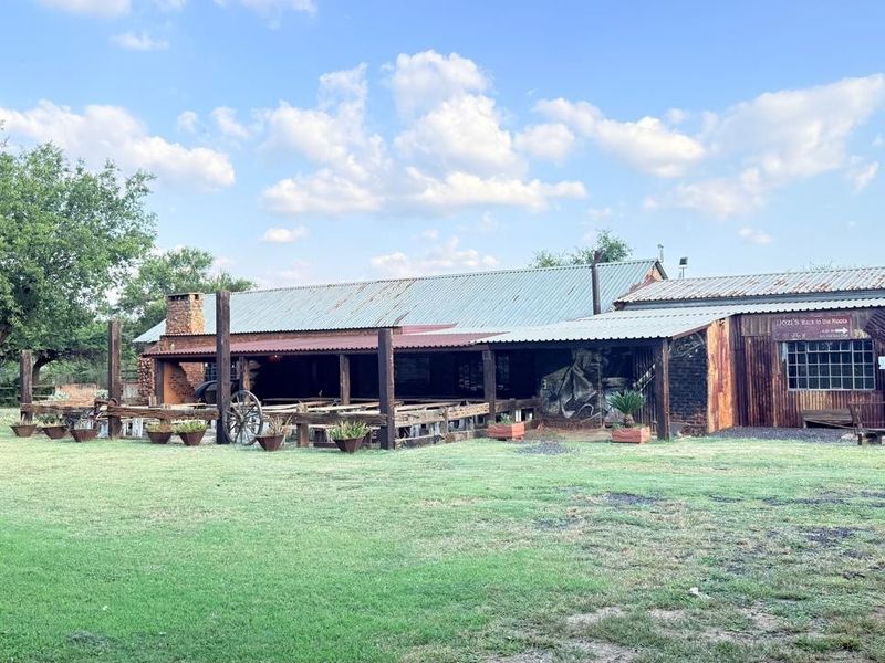 A rustic, industrial-style exterior rear view of a small holding building featuring corrugated metal finishes, a covered patio area, and a brick chimney.