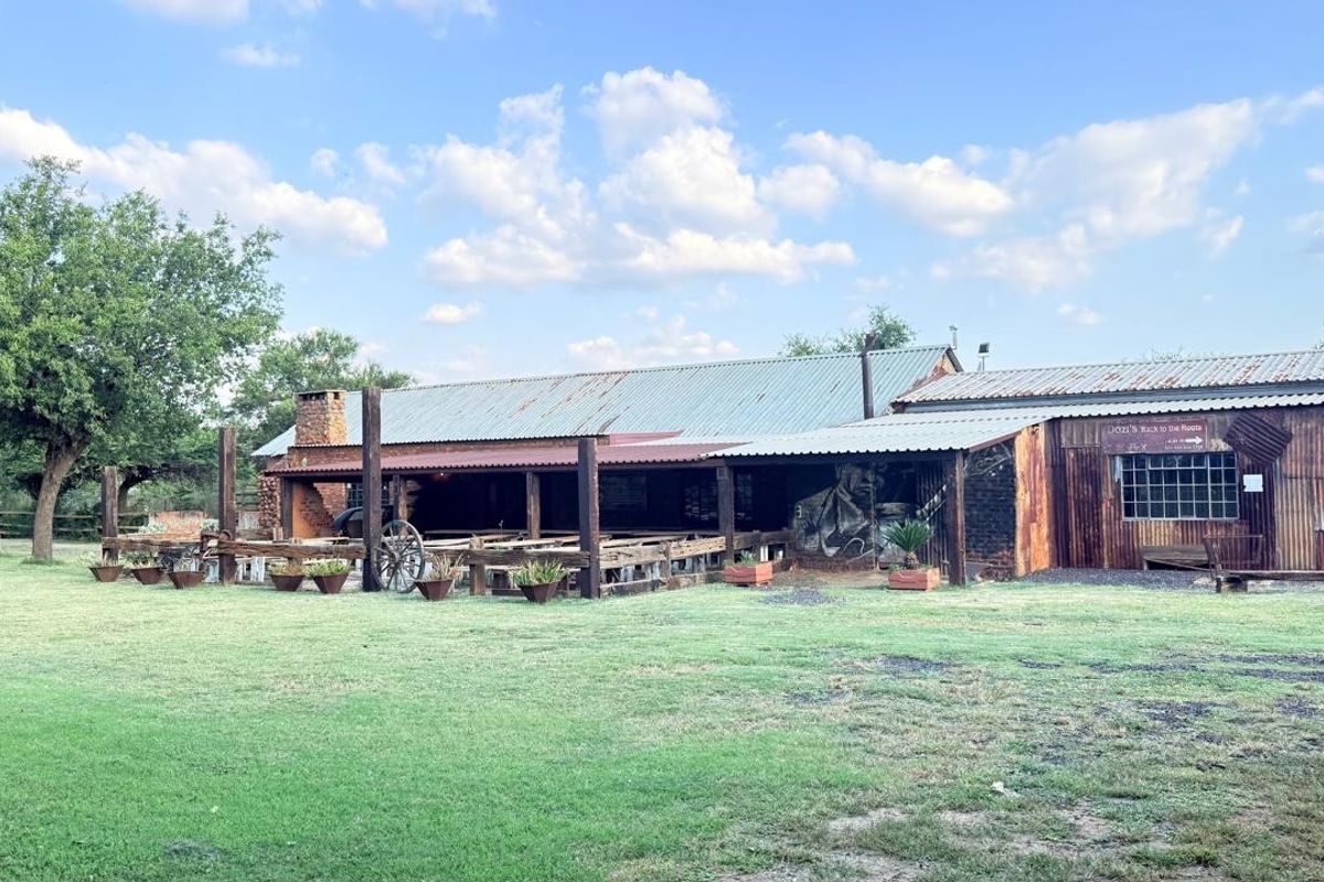 A rustic, industrial-style exterior rear view of a small holding building featuring corrugated metal finishes, a covered patio area, and a brick chimney.