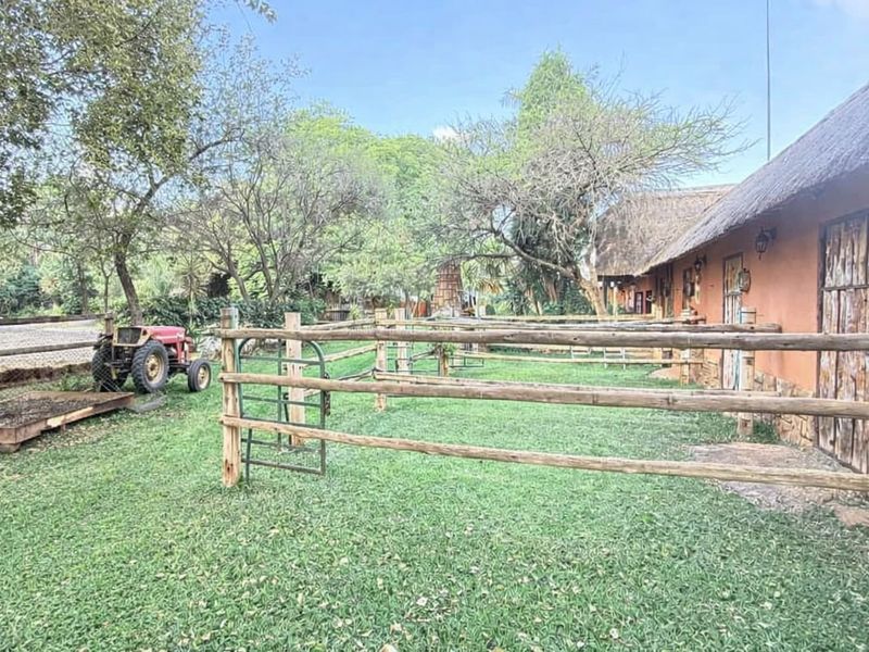 A rustic small holding exterior featuring a thatched roof building with stone cladding, surrounded by timber fencing and a well-maintained lawn area.