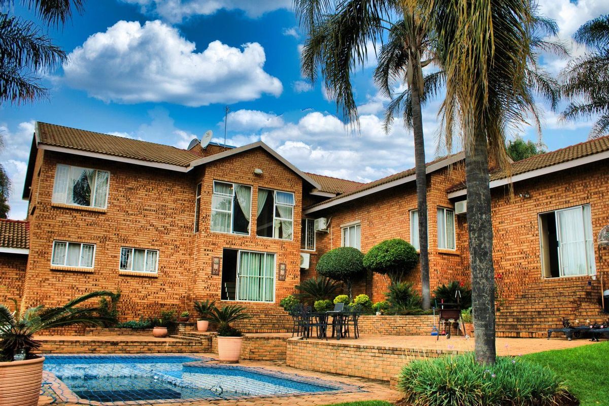 Rear view of a double-story brick house featuring a swimming pool, paved terrace area, and established garden landscaping.