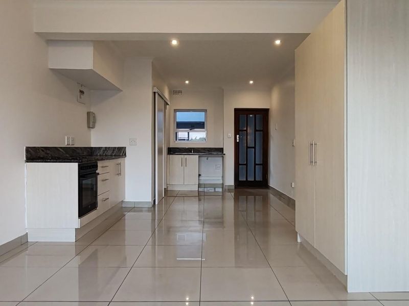 An open-plan living and kitchen area featuring tiled flooring, modern cabinetry, granite countertops, and built-in storage cupboards.