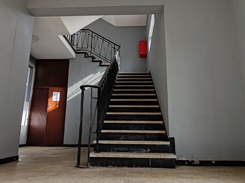 A communal apartment building entrance featuring a central staircase with metal balustrades and tiled flooring.
