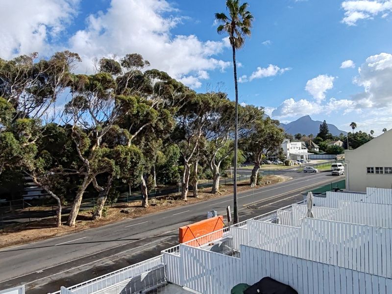 Elevated view overlooking the street, surrounding trees, and distant mountain landscape from the apartment balcony.