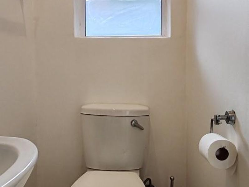 A compact bathroom featuring a standard toilet, wall-mounted washbasin, and tiled flooring, illuminated by a single window.