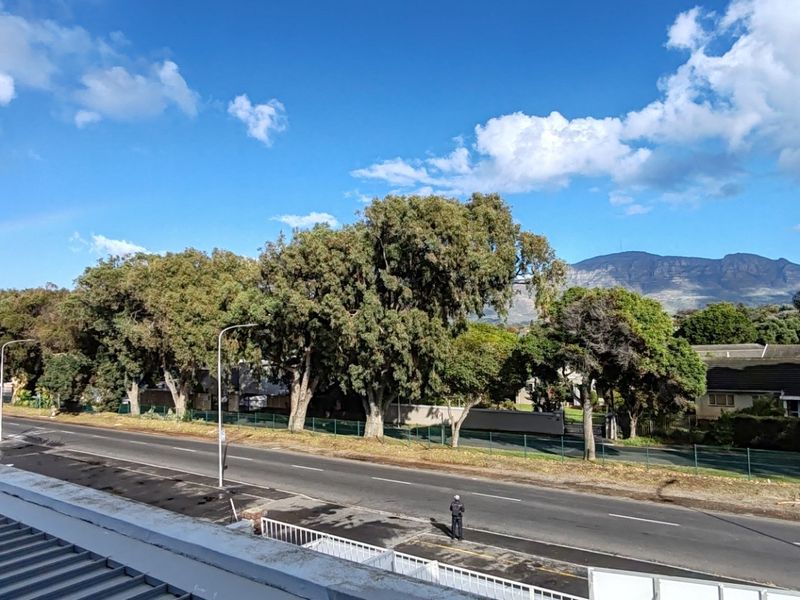 Elevated view overlooking a public road, mature trees, and distant mountain range, with a commercial property visible in the foreground.