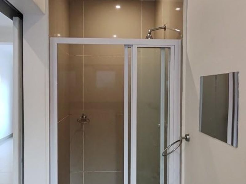 A compact bathroom featuring a tiled shower enclosure with a glass door and a white pedestal basin with a modern mixer tap.