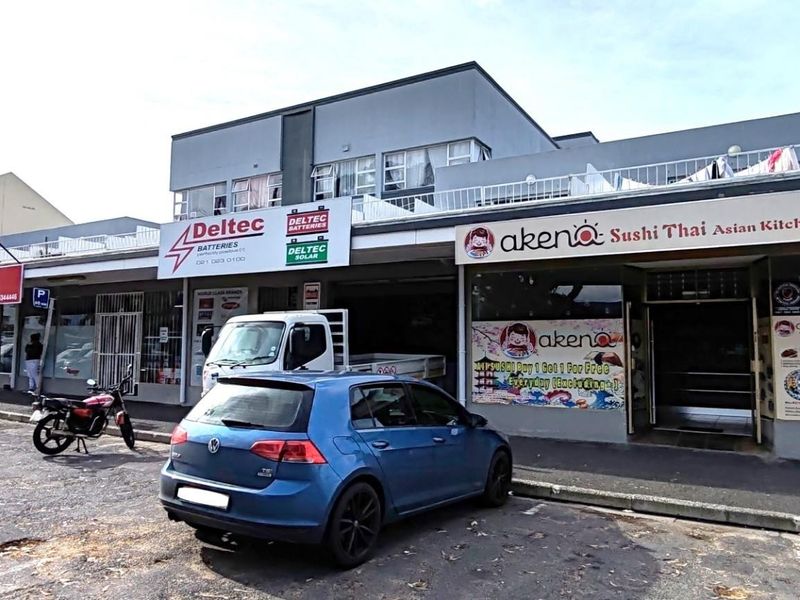 Front exterior view of a multi-unit commercial building featuring ground-level storefronts with signage and upper-level residential balconies.