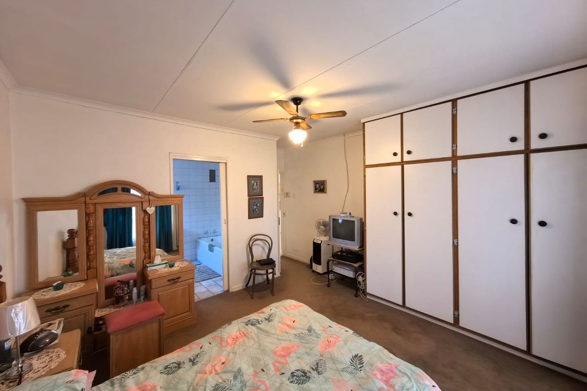 A spacious bedroom featuring extensive built-in floor-to-ceiling wardrobes and an adjoining en-suite bathroom.