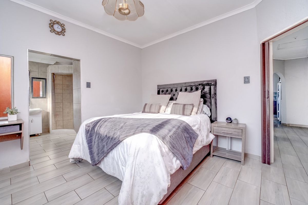 A well-maintained bedroom featuring light-toned floor tiles, a neutral color palette, and an adjoining en-suite bathroom.