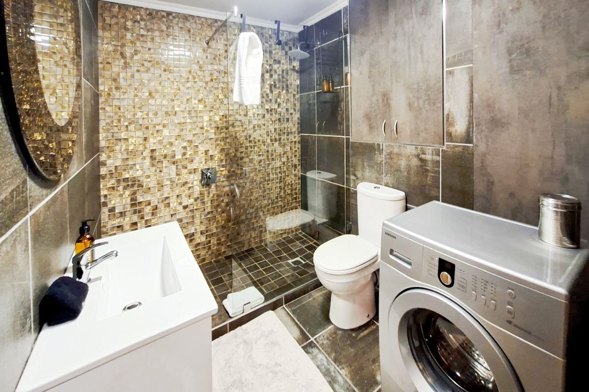 Modern bathroom featuring a walk-in shower with mosaic tiling, a sleek vanity, and integrated laundry space with built-in cabinetry.