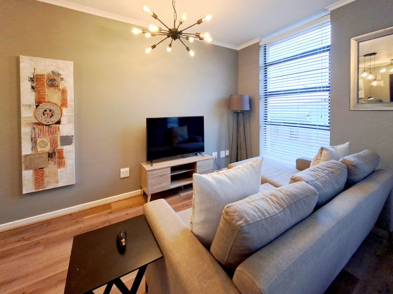 A well-maintained living room featuring laminate flooring, modern lighting, and large windows with venetian blinds, creating a bright and comfortable living space.