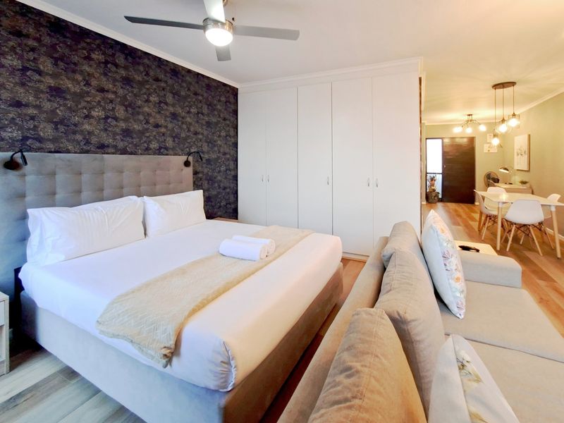 Spacious bedroom featuring built-in cupboards, a ceiling fan, and modern laminate flooring, with an open-plan layout leading to the dining area.