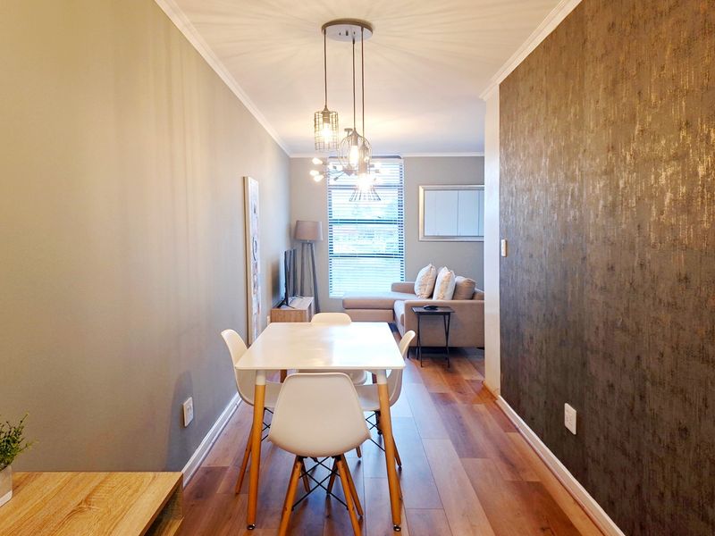 An open-plan living and dining area featuring laminate flooring, a textured feature wall, and modern pendant lighting with natural light from a large window.