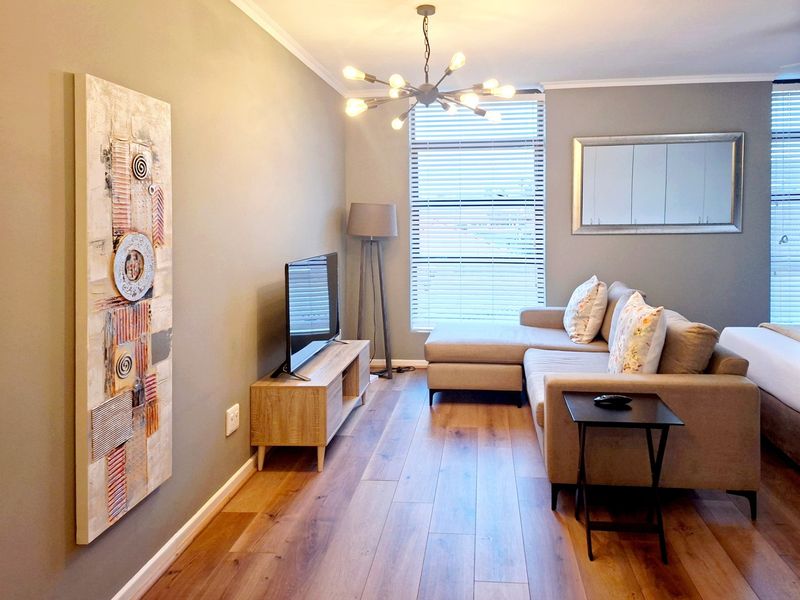 A well-maintained living area featuring modern laminate flooring, contemporary lighting, and large windows with venetian blinds, creating a bright and inviting space.