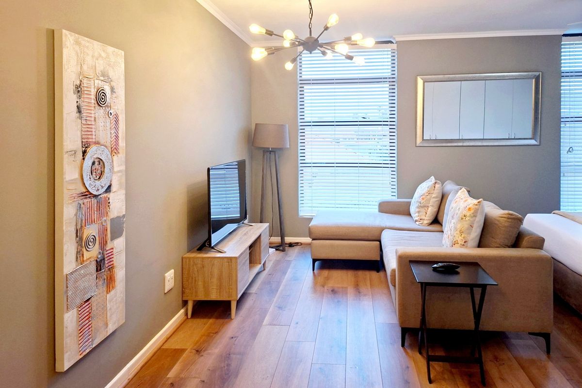 A well-maintained living area featuring modern laminate flooring, contemporary lighting, and large windows with venetian blinds, creating a bright and inviting space.