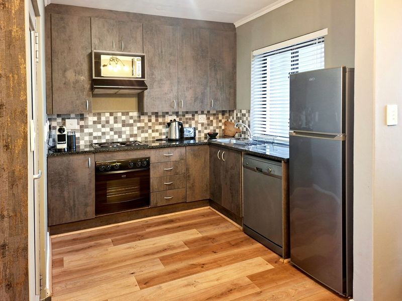 Modern kitchen featuring dark textured cabinetry, granite countertops, mosaic backsplash, built-in oven, hob, extractor fan, and integrated microwave with laminate flooring.